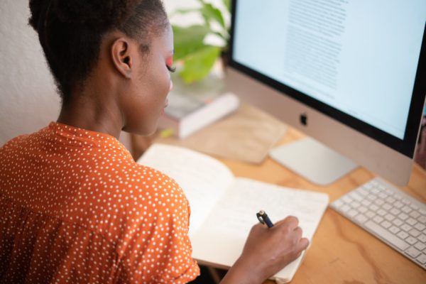 Student taking notes at computer desk